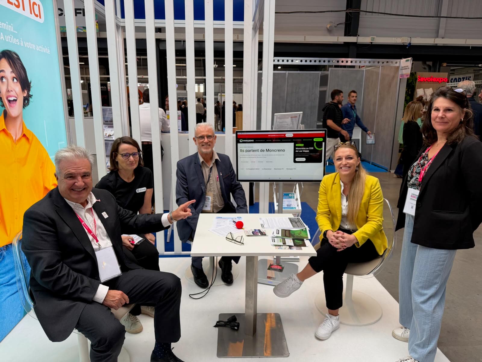 Cinq personnes réunies autour d’une table sur le stand de la CCI Savoie au salon Décidia, à Savoiexpo ; à l’écran, la page « Ils parlent de Moncreno » du site.